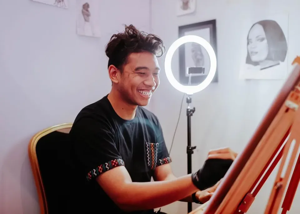 Furba Gurung smiling while drawing at an easel in his studio.